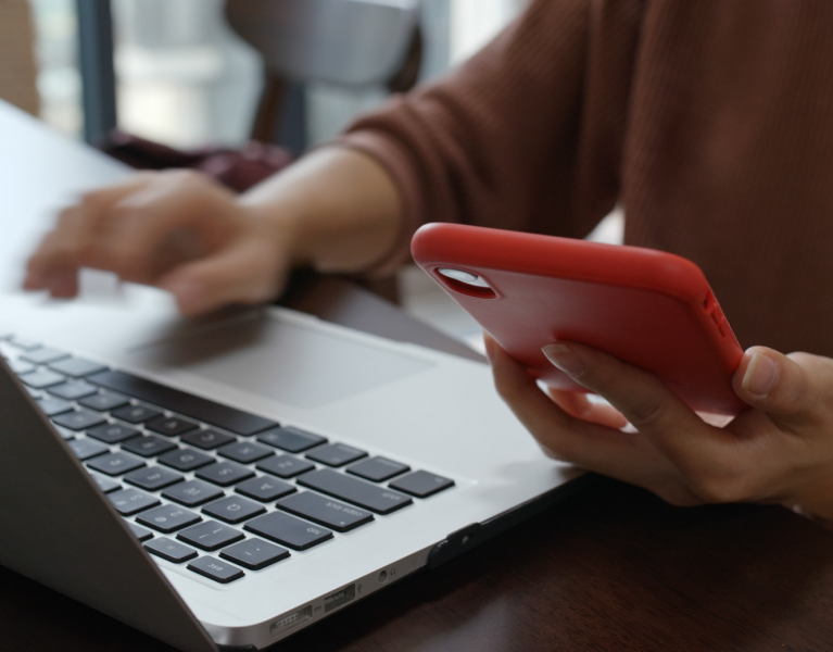 Woman working on computer whilst referencing their phone