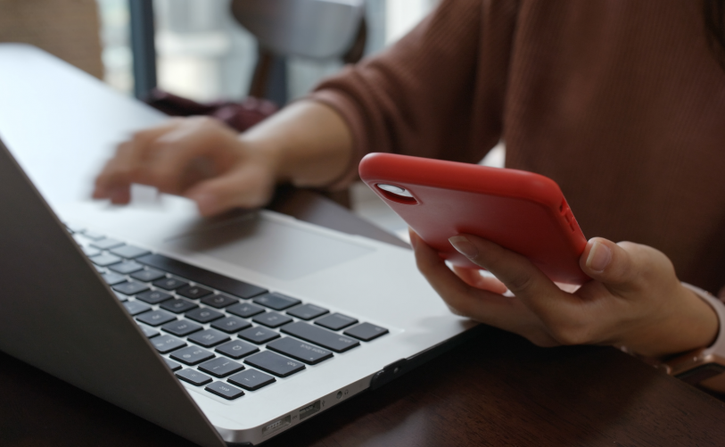 Woman working on computer whilst referencing their phone